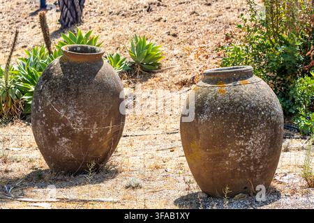 These large, rustic earthenware vessels show signs of age and exposure to the elements, standing on arid ground with sparse vegetation Stock Photo