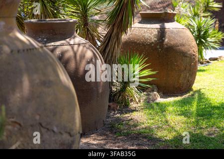 Three weathered terracotta pots with textured surfaces sit in a garden setting, casting shadows on the vibrant green lawn and surrounding foliage Stock Photo
