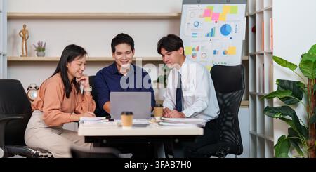 Asian business team collaborating around laptop in modern office for AI technology planning Stock Photo