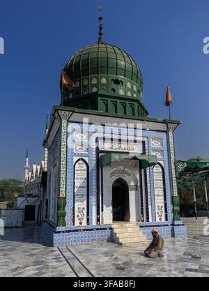 View of the Kamal Chishti Darbar with its iconic green dome and intricate blue and white tile work, featuring a man kneeling in prayer on the marble c Stock Photo
