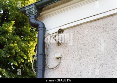 Security camera installed on a textured building wall beside a drainpipe for surveillance, monitoring, and perimeter safety protection, safety technology Stock Photo