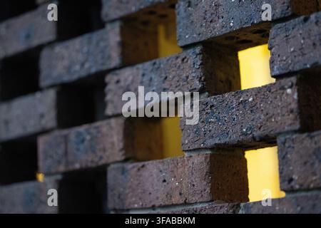 Close-up of dark brick screen wall with warm yellow light glowing through gaps, architecture and design detail with shallow depth of field Stock Photo