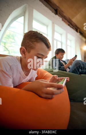 Focused school-age boy using smartphone with other children behind him Stock Photo