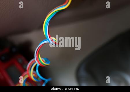 A colorful electrical wire coiled cable exposed conductor multicolor wire curled wire close up detail showing bright insulated strands hanging beside Stock Photo