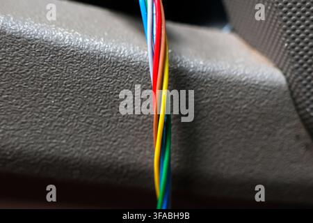 A colorful electrical wire bundle emerging from textured black plastic surface, showing red, blue, yellow, green, and white insulation with technical Stock Photo