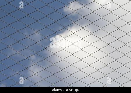 Chain link fence against a blue sky with white clouds. Stock Photo