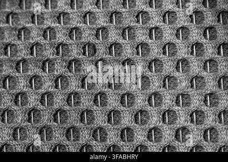 A gray knitted fabric texture with repeating open loops and woven fibers, creating detailed textile background pattern with tactile depth and monochro Stock Photo