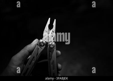 A multitool plier held in hand against dark background, creating practical repair and outdoor maintenance scene with strong monochrome contrast and fo Stock Photo