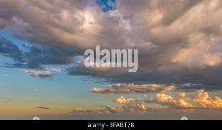 Beautiful evening sky filled with dramatic clouds illuminated by the golden light of the setting sun, ideal for background or replacement. Stock Photo