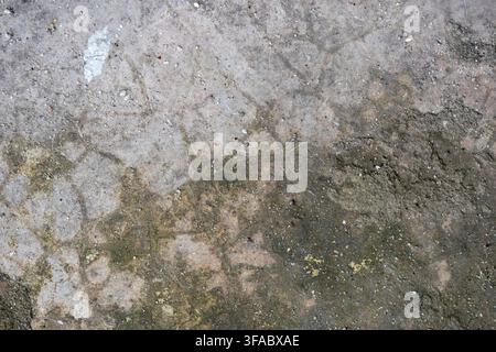 Weathered rough concrete floor surface displaying dark moisture stains and fine cracks. Aged cement flooring texture showing natural wear and surface Stock Photo