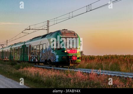 "Modern green regional train traveling through the Italian countryside on tracks at sunset" Stock Photo