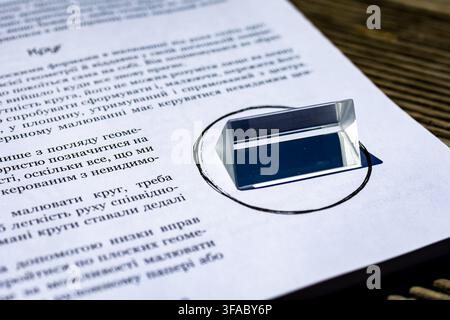 Triangular glass prism resting on a printed worksheet with a hand drawn circle. Sunlight creates reflections and soft shadows. Concept of optics study Stock Photo
