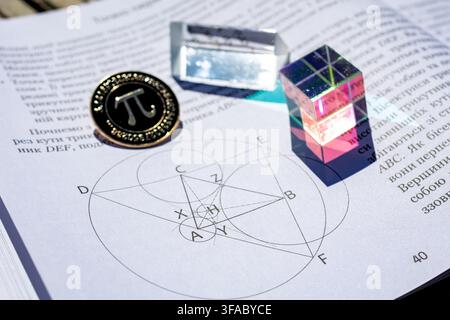 Pi coin a rectangular prism and a colorful cube arranged on a math text with geometric diagrams in sunlight illustrating optics study creativity geome Stock Photo