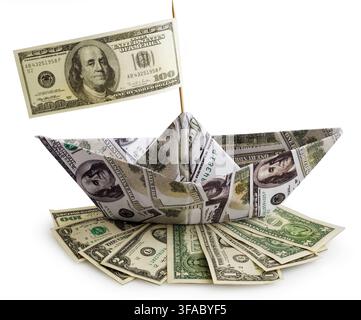 Conceptual financial image of an origami ship made from US dollar banknotes with a 100 dollar bill flag, resting on a pile of various US currency bill. Stock Photo