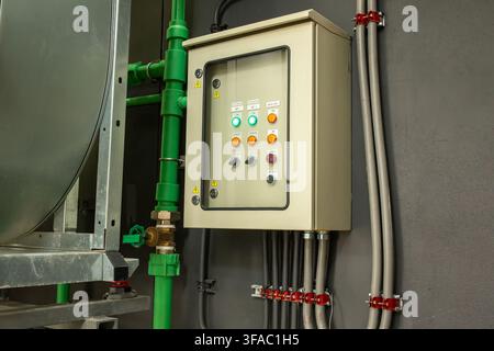 Industrial electrical control panel with buttons and indicator lights mounted on wall near pipes, automation equipment concept Stock Photo