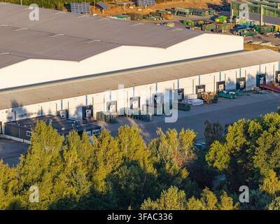 Aerial view of a modern logistics warehouse featuring multiple loading docks, industrial containers, and surrounding greenery in Genk, Flanders, Belgi Stock Photo