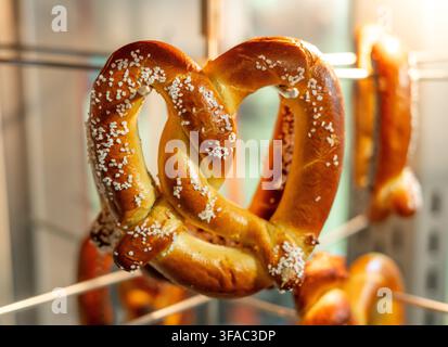 Large Hot Soft Salted Pretzels hanging in a glass display ready to serve Stock Photo
