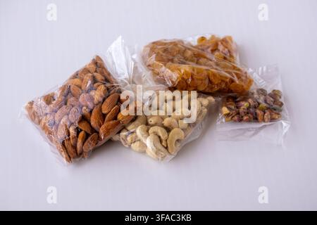 Assorted dry fruits packed in transparent plastic pouches placed on white background. Raw almonds, cashews, raisins, and pistachios packaged for healt Stock Photo