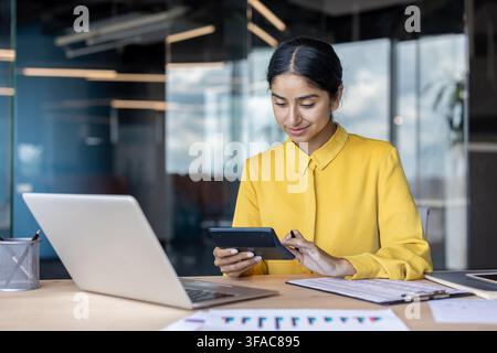 Concentrated young Indian woman working in office with documents and using calculator. Stock Photo