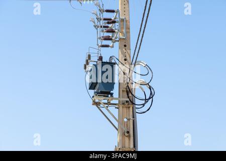 A dark blue electrical transformer is attached to a concrete utility pole with various wires and insulators Stock Photo