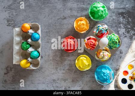 Top view of colorful marbled Easter eggs arranged with watercolor paints and craft supplies on a gray textured background creating a vibrant spring ho Stock Photo