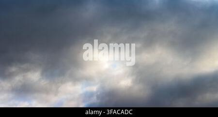 Dramatic sky filled with dark, swirling clouds. Sunlight breaks through in soft, diffused beams. Mood evokes anticipation or stormy change. Ideal for Stock Photo