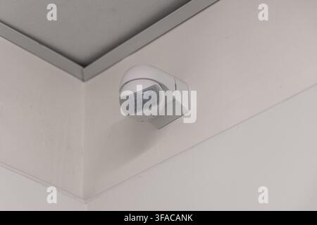 A modern white motion detector is installed on a wall near the ceiling, indicating a security or automation system Stock Photo