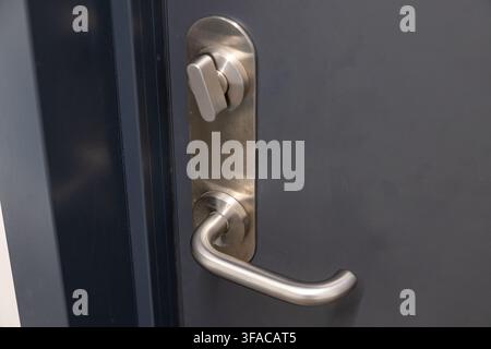 Close-up view of a contemporary brushed stainless steel door handle and a rotating lock mechanism set against a matte dark gray door surface Stock Photo