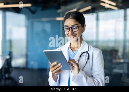 Smiling Indian female doctor standing in hospital room and using tablet. Stock Photo
