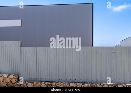 A minimalist composition featuring the gray corrugated metal exterior of a modern industrial building behind a similar fence and a rustic stone base Stock Photo