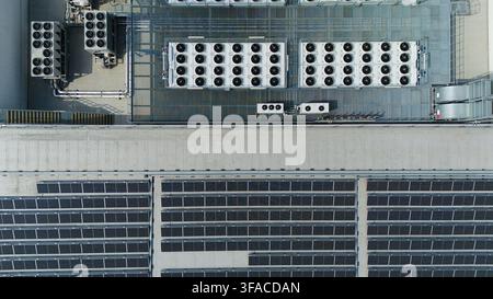 Aerial view of industrial rooftop featuring multiple ventilation cooling units, heat exchangers, HVAC fans, and rows of solar panels in Luton, England Stock Photo