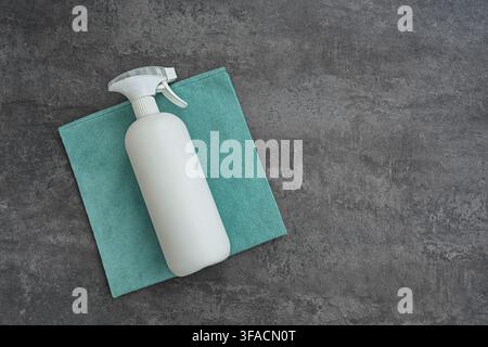 Blank white spray bottle and microfiber cleaning cloth on dark gray background, cleaning supplies flat lay with large copy space. Stock Photo