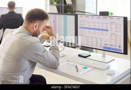 Stressed financial analyst man at computer in modern office with spreadsheets Stock Photo
