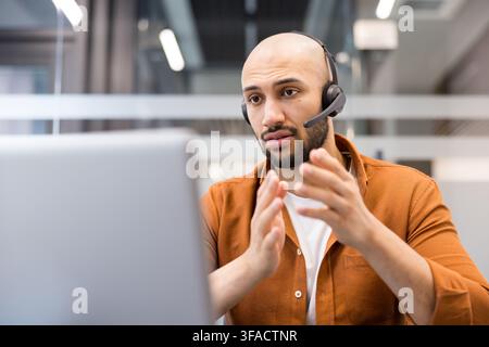 Customer support agent wearing a headset and actively talking on a video call, providing assistance or technical support from an office environment, demonstrating professional remote communication Stock Photo