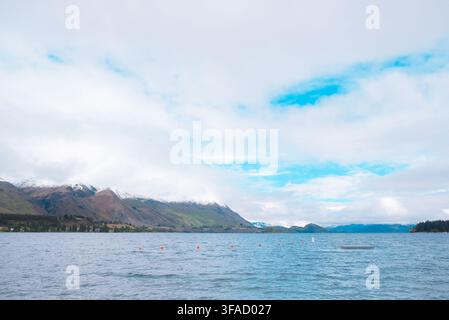 Wanaka, New Zealand: wide view across the lake with gentle water ripples toward snow capped mountain peaks under cloudy skies, South Island vacation Stock Photo