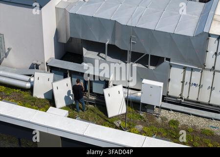 Aerial view of a technician inspecting electrical panels near a large industrial cooling and hvac system on a green roof in Krakow, Lesser Poland Voiv Stock Photo