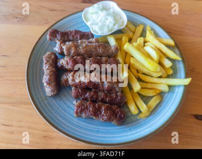 Plate of grilled cevapi, golden french fries, and chopped raw onion, a traditional Balkan meal in Skopje, North Macedonia Stock Photo