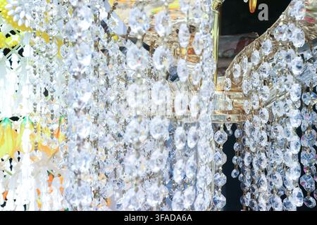 Sparkling faceted crystal beads hang from a Thai style chandelier, catching warm light in close up view. Stock Photo