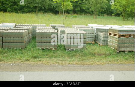 Concrete paving blocks stacked interlocking pavers rectangular, bricks curb blocks stacked wooden pallets green plastic banding straps strapping Stock Photo