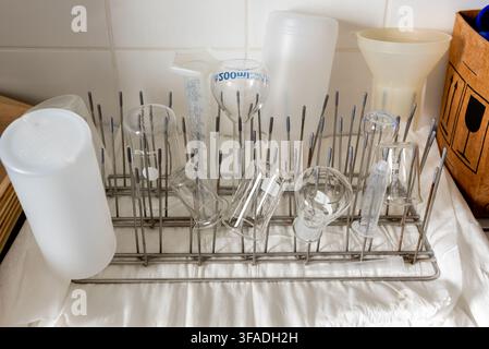 Laboratory glassware, including beakers, flasks, graduated cylinders, and funnels, drying upside down on a metal peg rack in chemistry lab. The clean, Stock Photo
