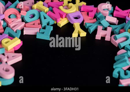 Colorful wooden letters are spread out on a black surface. Stock Photo