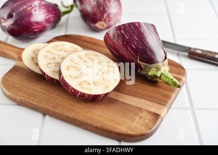 Three fresh purple eggplants  on wooden cutting board with knife on light background, closeup Stock Photo