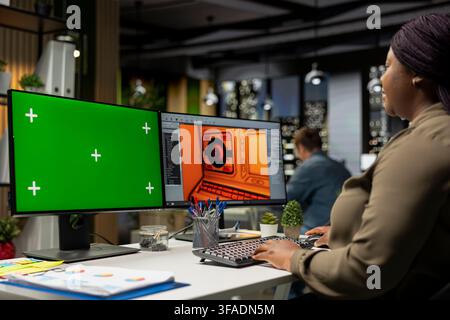 Black woman employee works on game development with chroma key, using dual monitors at the office. Female expert engineer creating a futuristic spaceship station on modern software. Stock Photo