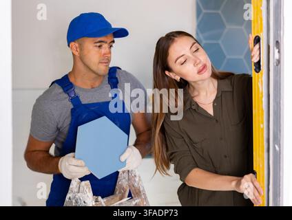 Woman using spirit level on wall with repairman Stock Photo