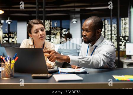 Team of office clerks completing spreadsheets on laptop, analyzing data, brainstorming. Teamworking colleagues browsing internet on notebook, researching information online, working overnight Stock Photo