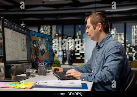 Expert designer decorating apartment floor plan using blueprints on pc, using architectural software to configure elements. Focused man uses interface to enable rendering and 3D modeling. Stock Photo
