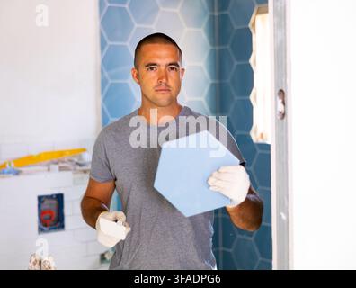 Skilled man builder in ordinary clothes posing with ceramic tiles while repair and decoration in apartment Stock Photo