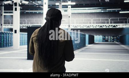 Woman walking through data center server rows, implementing advanced cooling and power management solutions. IT expert overseeing server farm, reducing energy consumption, camera A Stock Photo