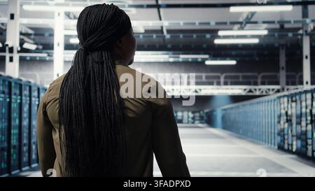 Admin in data center workplace overseeing large scale IT electronics to maintain seamless operations. Woman walking in high tech server room, doing network management for increased uptime, camera A Stock Photo