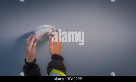 Close-up of a person installing or adjusting a smoke detector on a residential ceiling, representing home safety, fire prevention, maintenance, and se Stock Photo